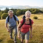 Senior Couple Climbing Hill On Hike Through Countryside Together